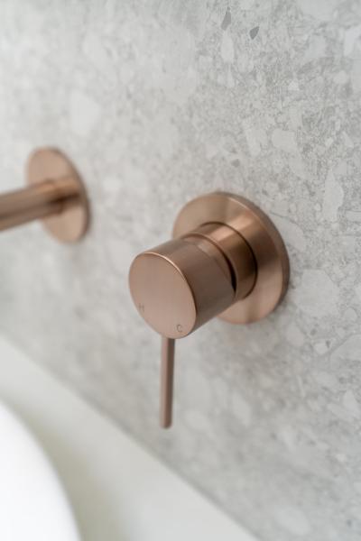 Brushed brass wall-mounted bathroom mixer tap on textured stone-look wall