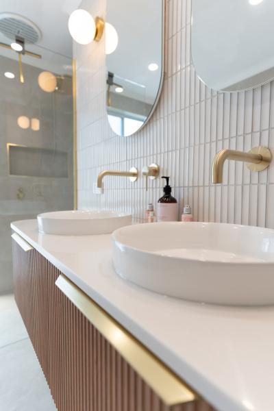 Modern bathroom vanity with twin basins, brass tapware and vertical white wall tiles