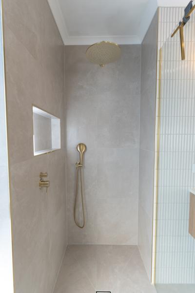 Minimalist walk-in shower with brass tapware, niche and pale grey wall tiles