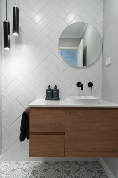 Modern bathroom vanity with round mirror, white basin and herringbone wall tiles