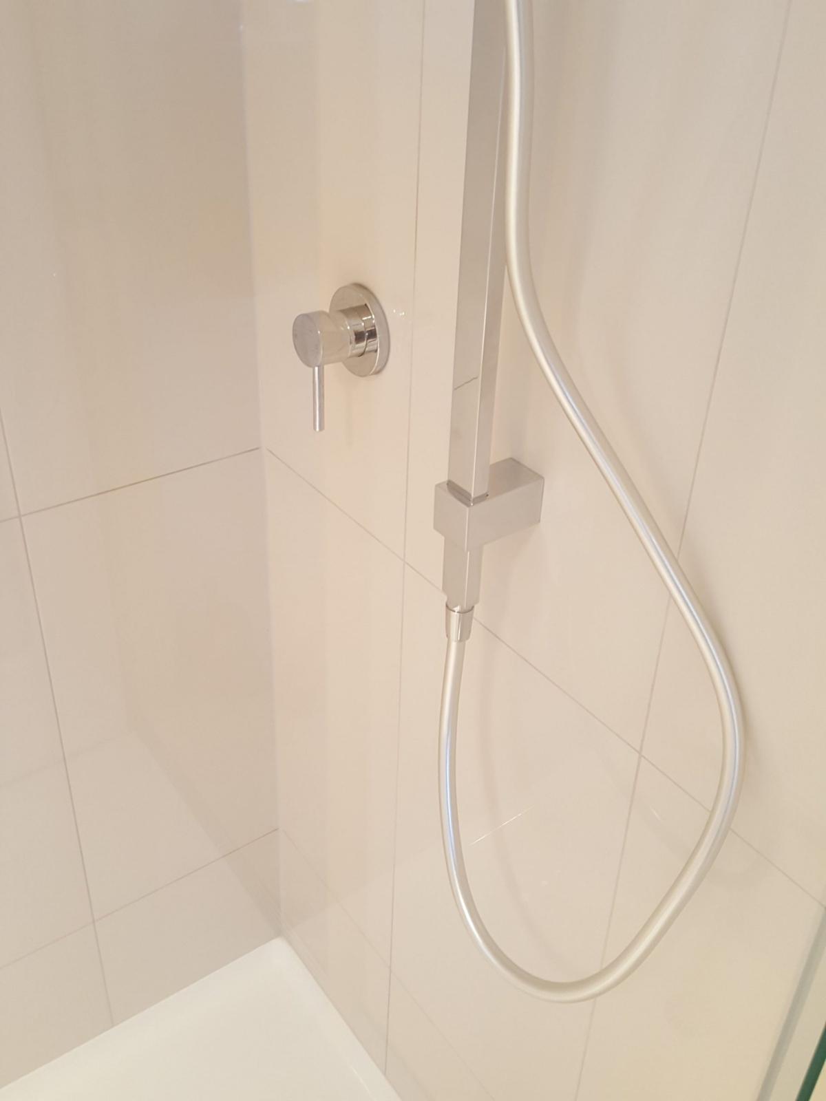 Modern chrome shower mixer with curved hose on white tiled wall