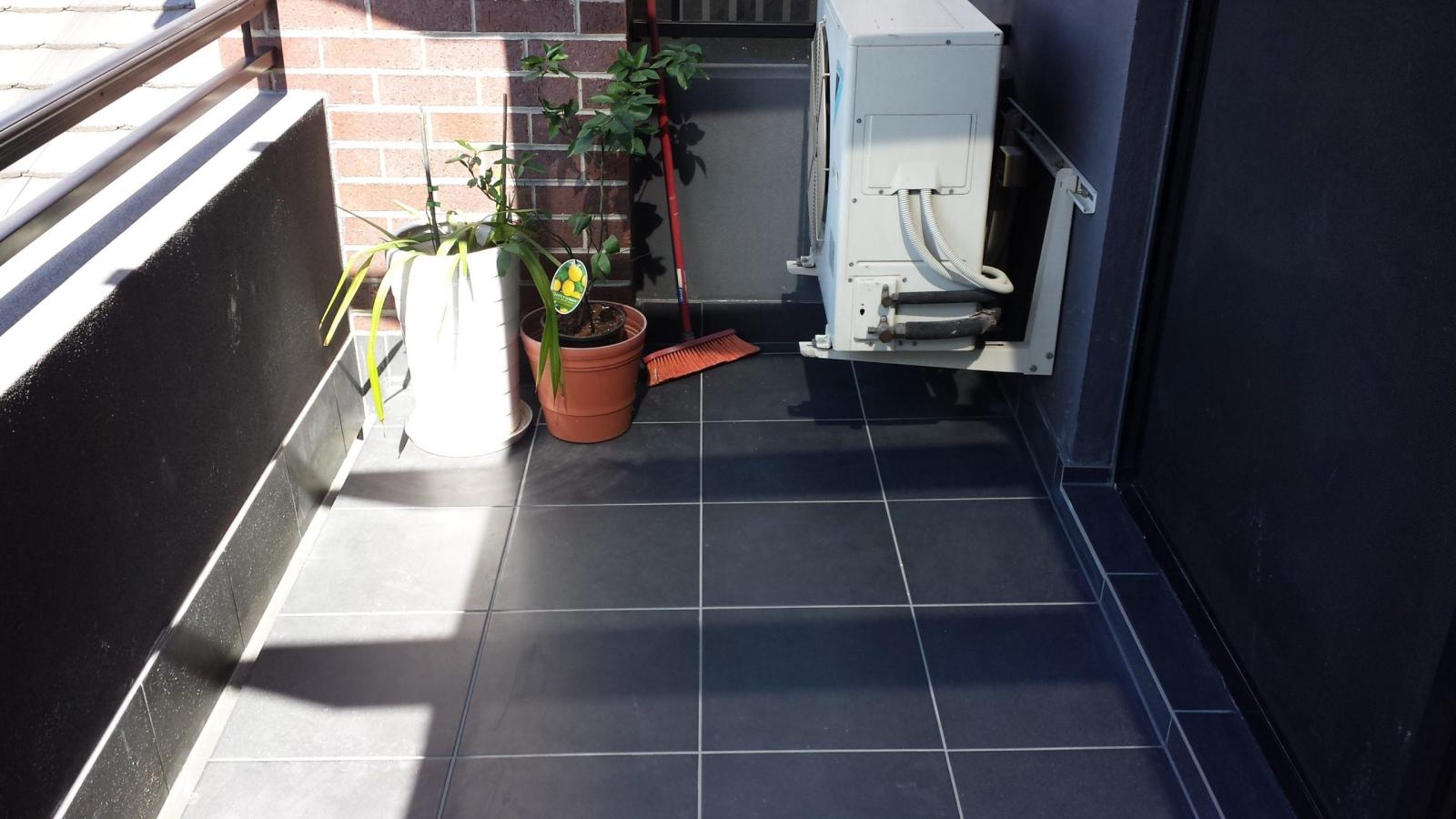 Tiled apartment balcony with dark floor tiles, potted plants and outdoor air conditioning unit
