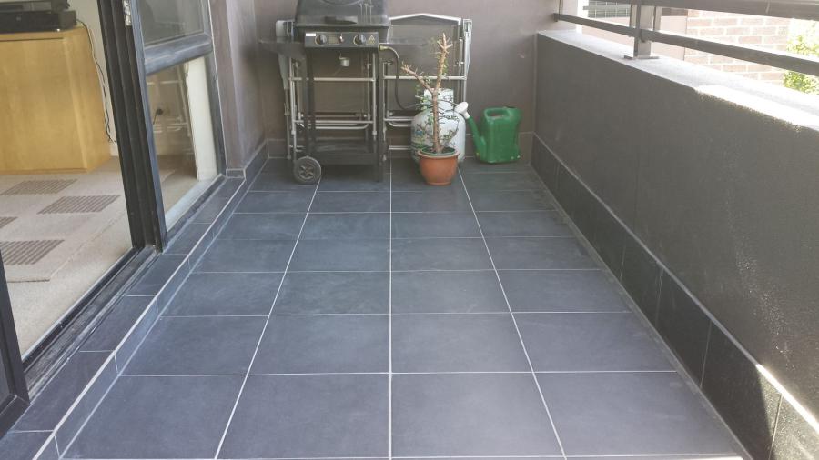 Grey tiled balcony with drainage grate, barbecue trolley and potted plant beside sliding doors