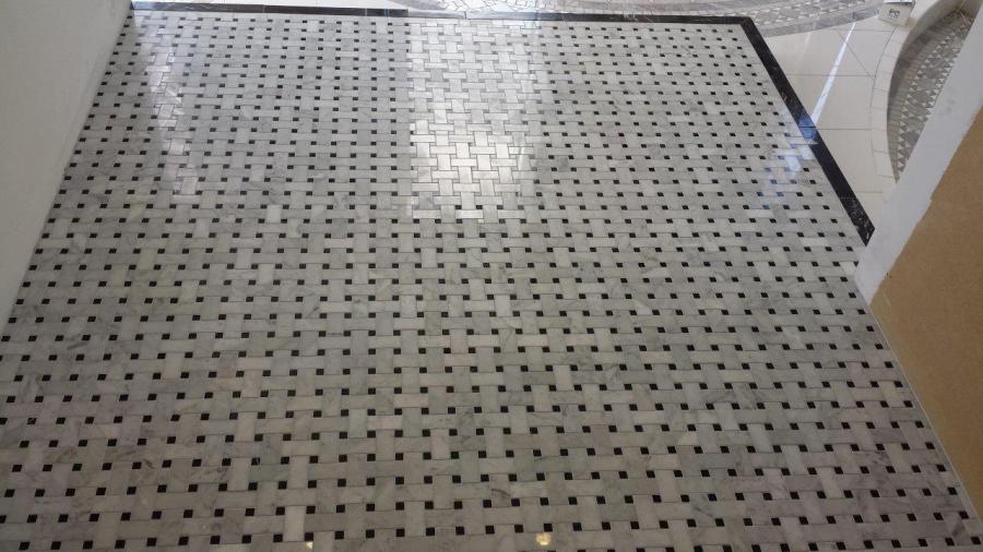 White tiled shower base with black mosaic pattern and linear floor waste