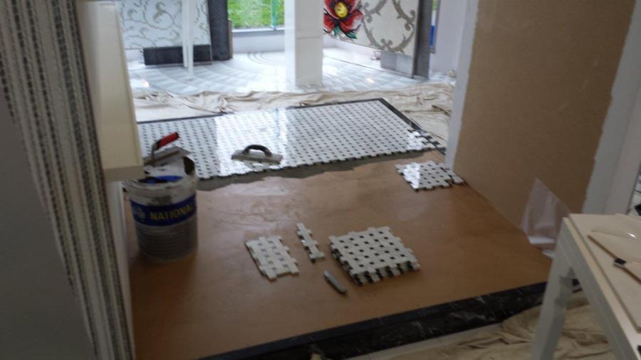 Bathroom renovation in progress with floor tiling laid and tools set out near an open doorway