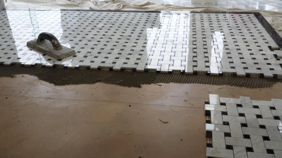 Bathroom floor tiling underway with white mosaic sheets being laid into fresh mortar