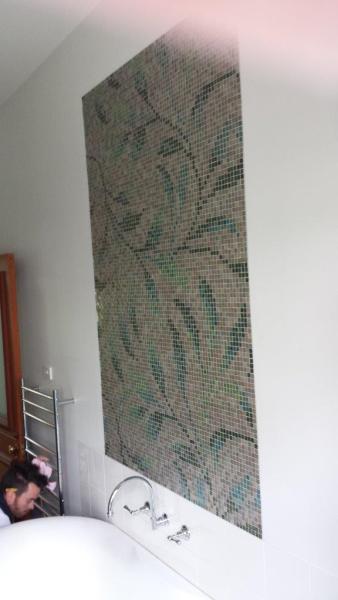 Tradesperson installing a tall floral mosaic tile feature wall in a bathroom