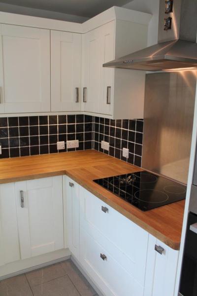 White kitchen cabinetry with timber benchtops, black tiled splashback and stainless steel rangehood