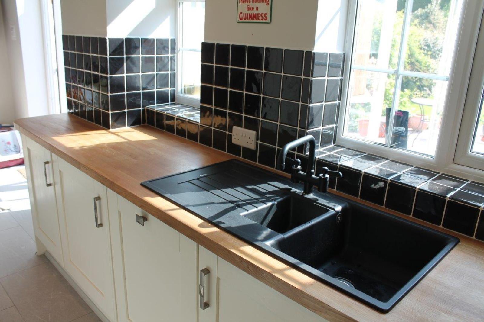 Black double kitchen sink with timber benchtop and white cabinetry beside a sunlit window