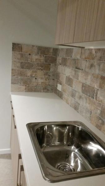 Compact laundry bench with stainless steel sink and stone-look tiled splashback