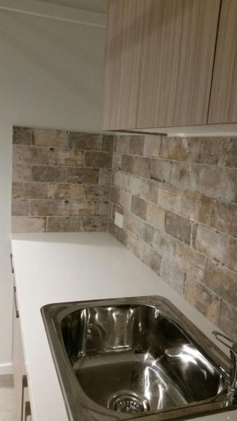 Compact laundry benchtop with stainless steel sink and beige tiled splashback