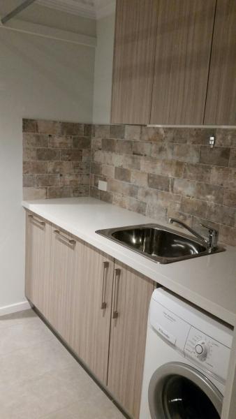 Compact laundry with timber-look cabinets, benchtop sink and front-loading washing machine