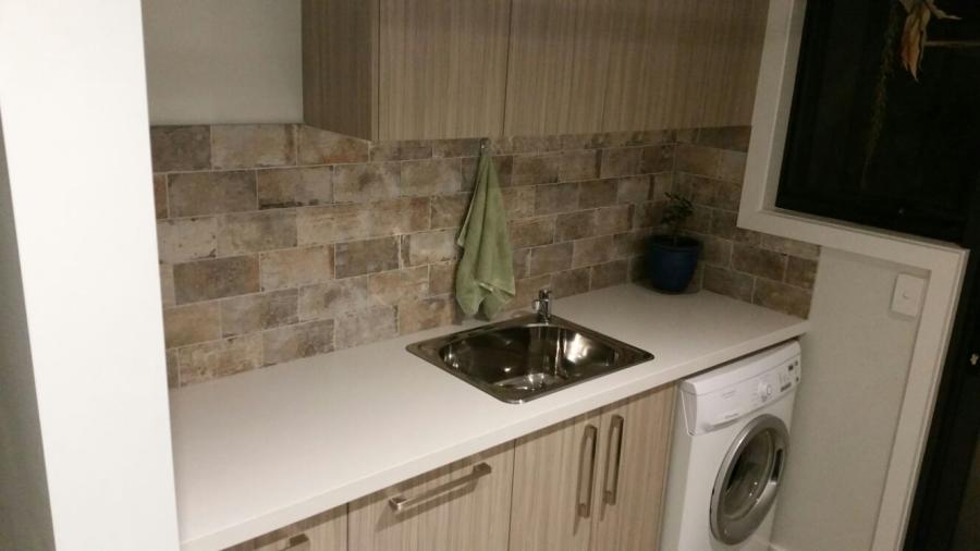 Compact modern laundry with sink, white benchtop, tiled splashback and front-loading washing machine