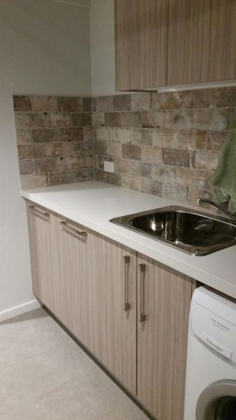 Compact laundry with timber-look cabinetry, stone-look splashback and inset sink