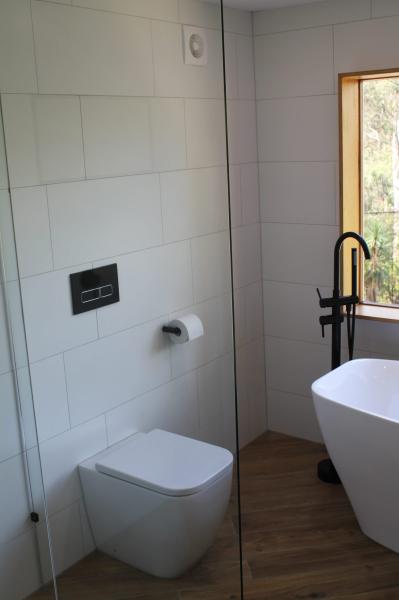 Modern white tiled bathroom with wall-hung toilet, freestanding bath and black floor-mounted tap