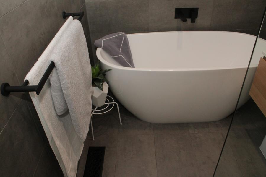 Modern bathroom with freestanding bath, grey tiles and black towel rail