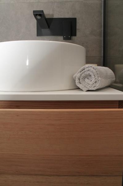White round basin on timber vanity with black wall tap and rolled hand towel