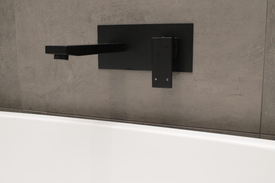 Matte black wall-mounted bath spout and mixer above a white bathtub with grey bathroom tiles