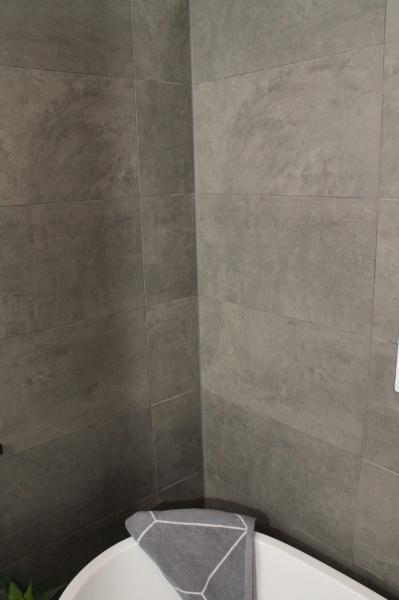 Grey tiled bathroom corner above a bathtub with large-format wall tiles