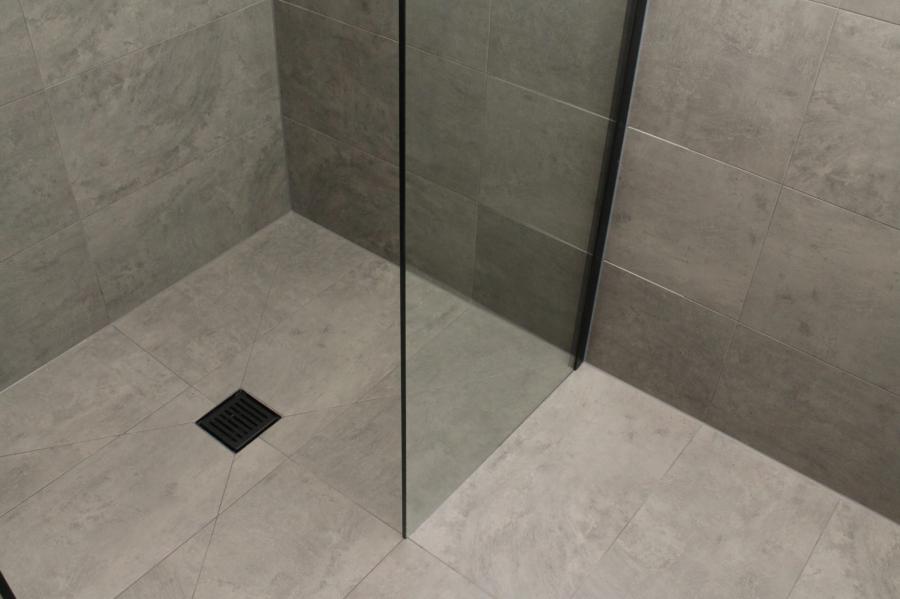 Frameless glass walk-in shower with grey floor tiles and square black floor waste