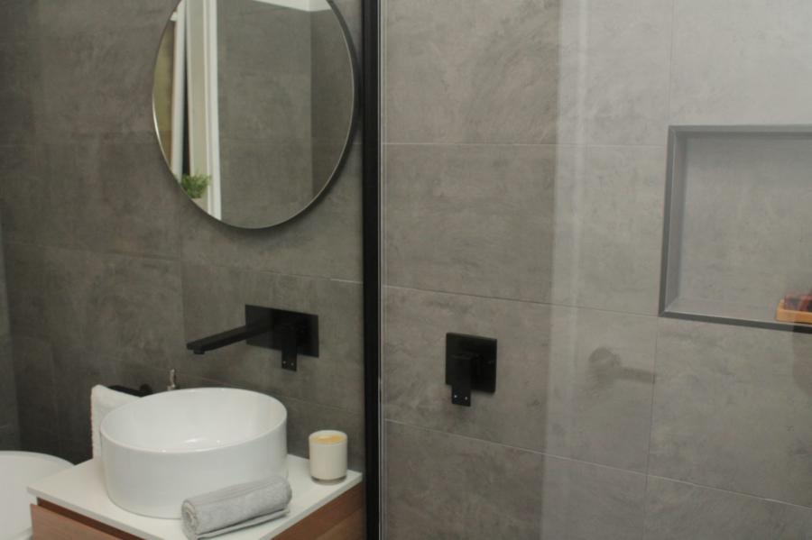 Modern grey tiled bathroom with round basin, black tapware and walk-in shower niche