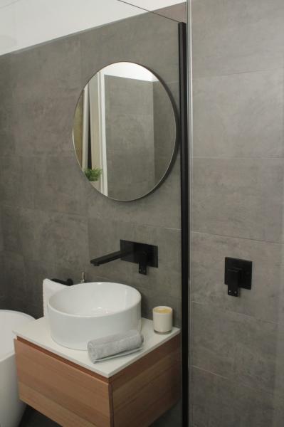Modern bathroom vanity with round mirror, vessel basin and grey tiled wall