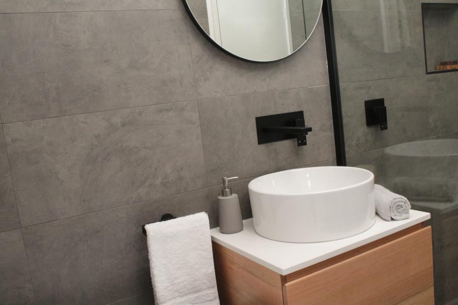 Modern bathroom vanity with round basin, black tapware and grey tiled walls