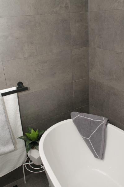Freestanding white bath with grey towel in a modern grey tiled bathroom