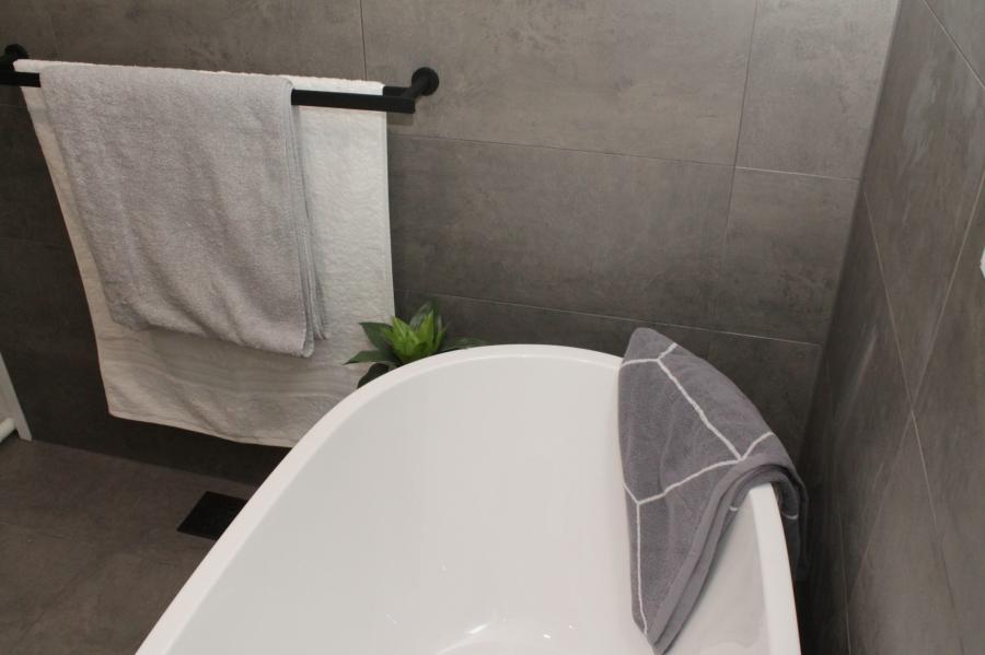 Modern white bathtub in a grey tiled bathroom with towel rail and folded hand towel