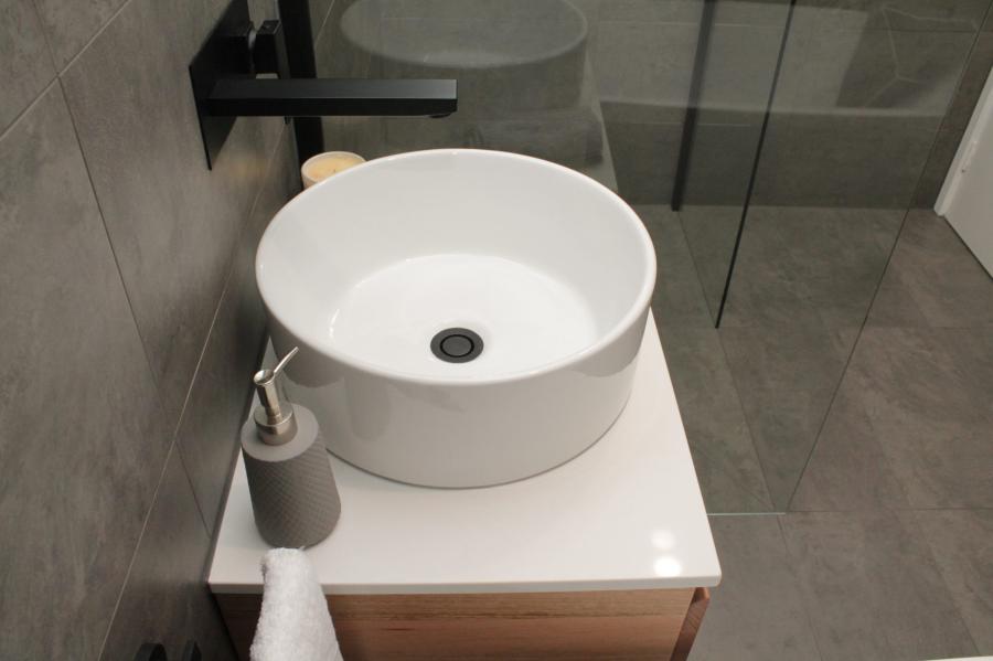 Round white basin on a compact vanity beside a glass shower in a modern grey bathroom