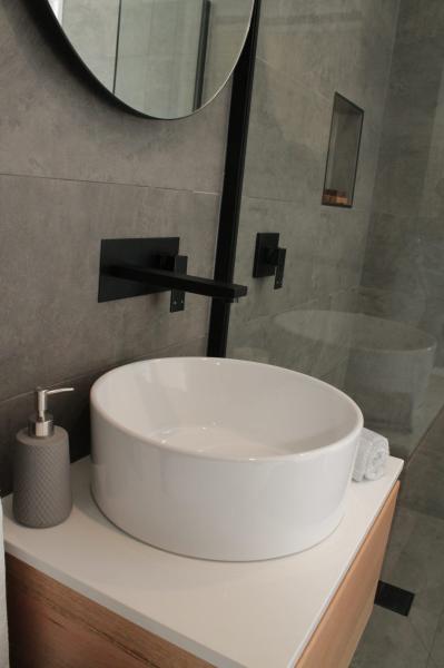 Modern bathroom vanity with round basin, black tapware and tiled shower niche
