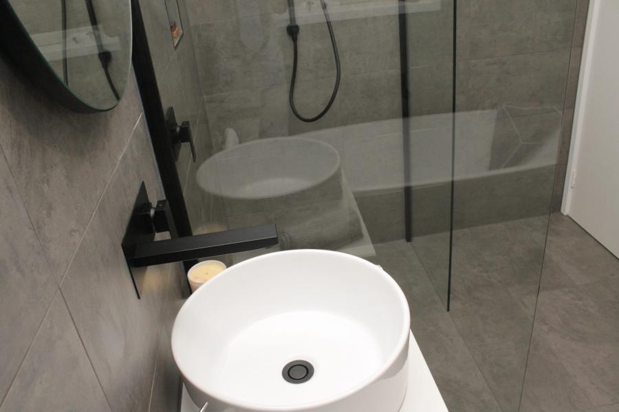 Modern bathroom with round basin, black tapware, walk-in shower and bathtub behind glass screen