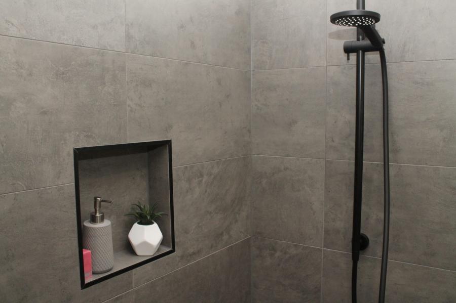 Grey tiled shower wall with recessed niche and black shower rail
