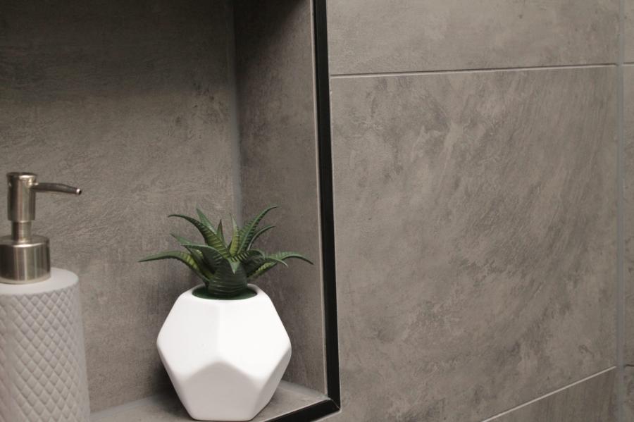 Built-in bathroom niche with plant and soap dispenser beside grey wall tiles