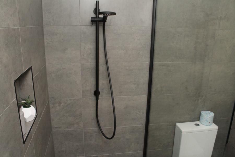 Modern grey tiled bathroom with black shower, recessed niche and glass screen