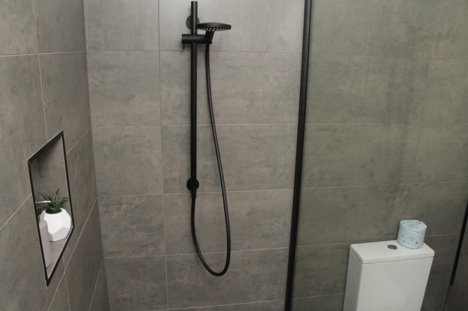 Modern grey tiled bathroom with black shower, recessed niche and glass screen