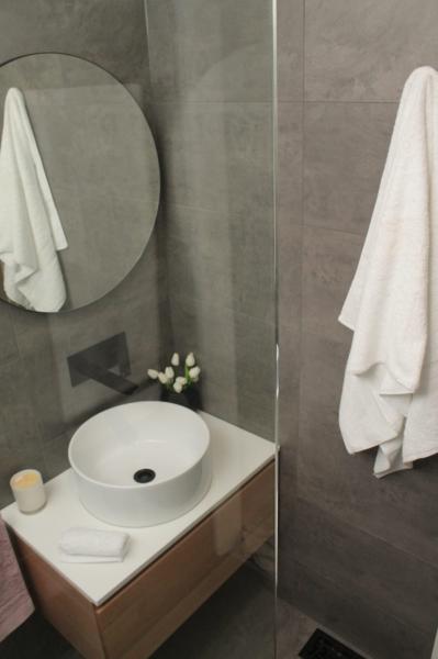 Modern bathroom vanity with round mirror, vessel basin and grey tiled walls