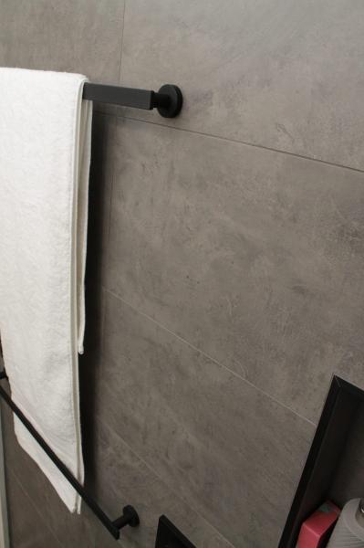 White towel on black rail against grey tiled bathroom wall