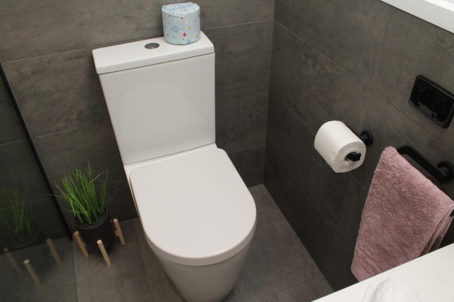 Modern white toilet with grey wall tiles, black fittings and pink hand towel