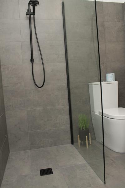 Walk-in shower with grey tiles, black shower rail and clear glass screen beside a modern toilet
