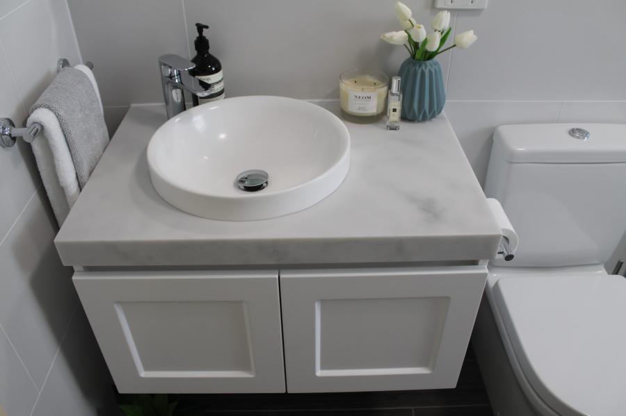 Compact white bathroom vanity with vessel basin beside toilet