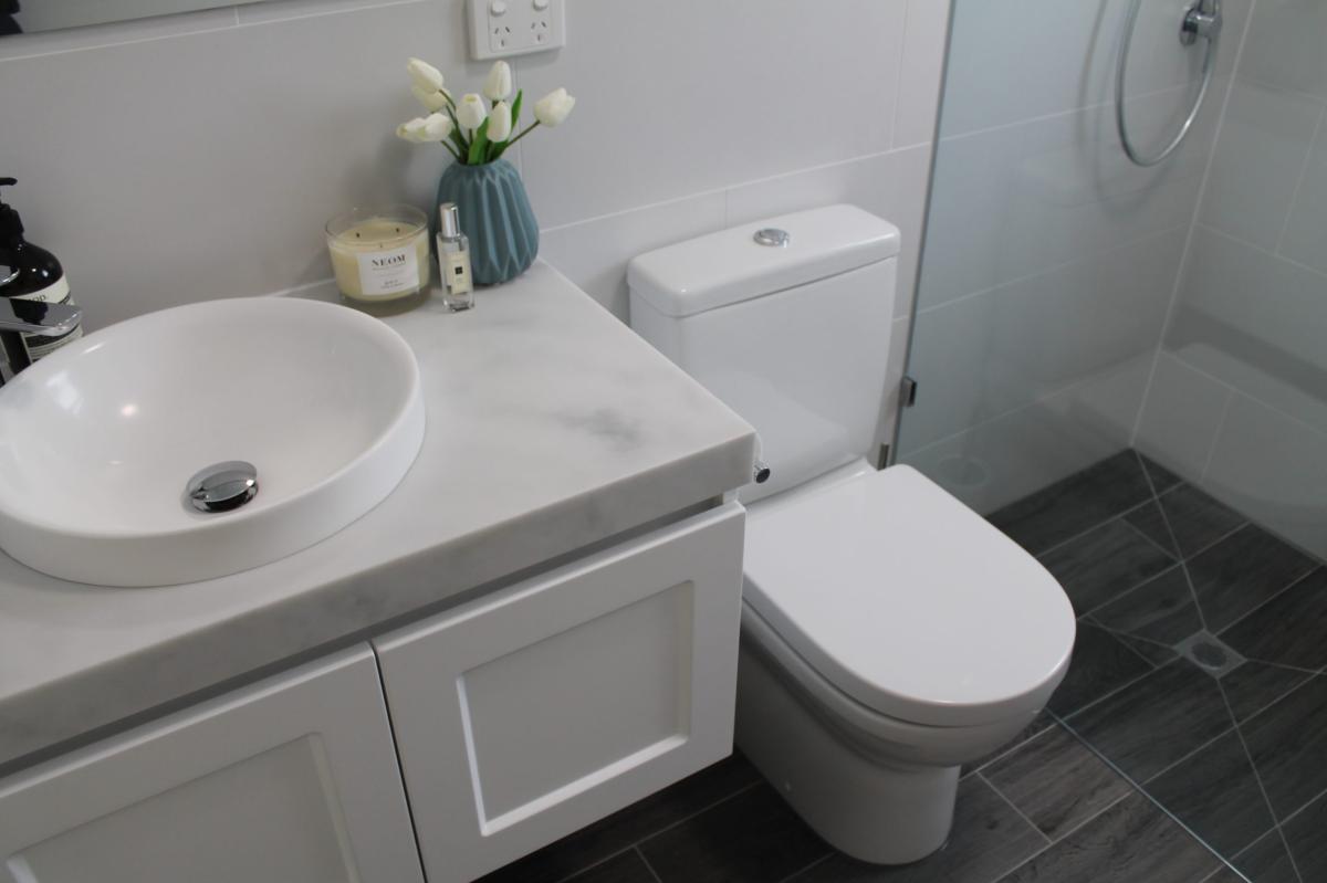 Modern white bathroom vanity, toilet and glass shower with grey floor tiles