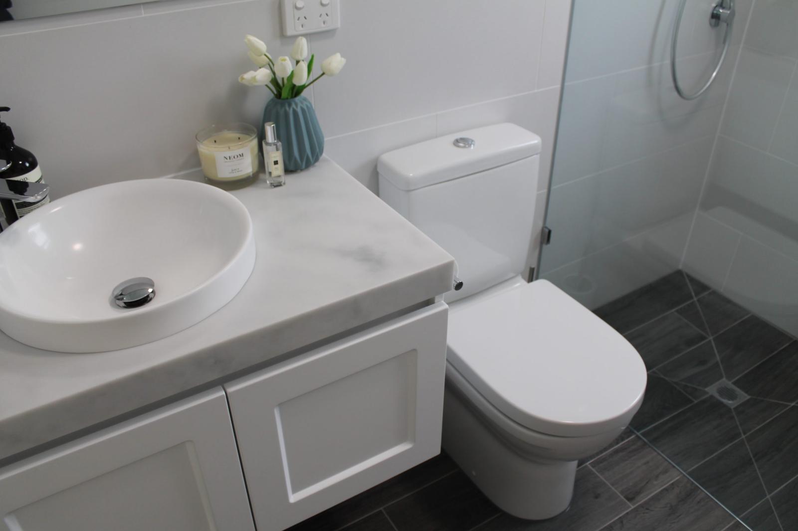Modern white bathroom vanity, toilet and glass shower with grey floor tiles