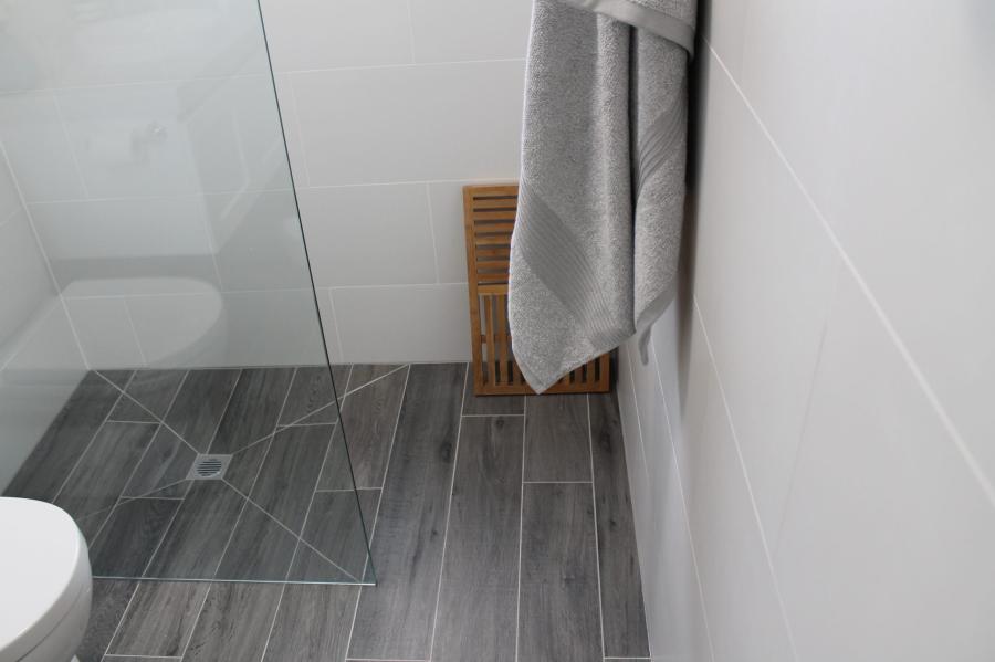 Grey tiled shower area with frameless glass screen and towel rack in a modern bathroom