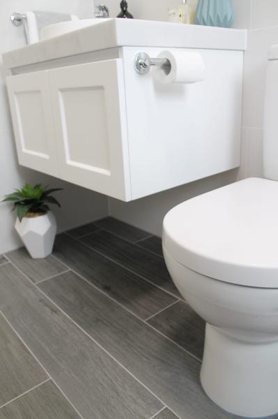 Wall-hung white bathroom vanity beside toilet with grey floor tiles