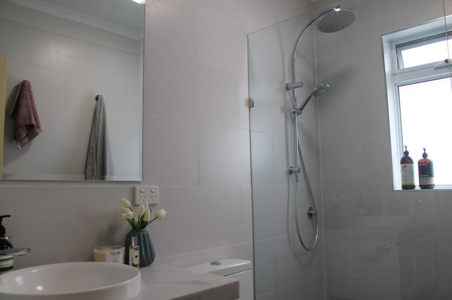 Modern white bathroom with glass shower, wall-mounted showerhead, mirror and basin