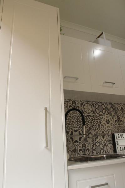 White laundry cabinetry with patterned tiled splashback and black gooseneck tap
