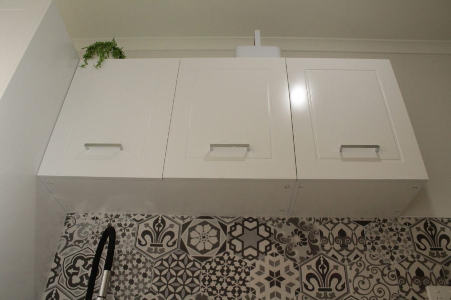 White wall-mounted laundry cabinets above patterned grey tiled splashback