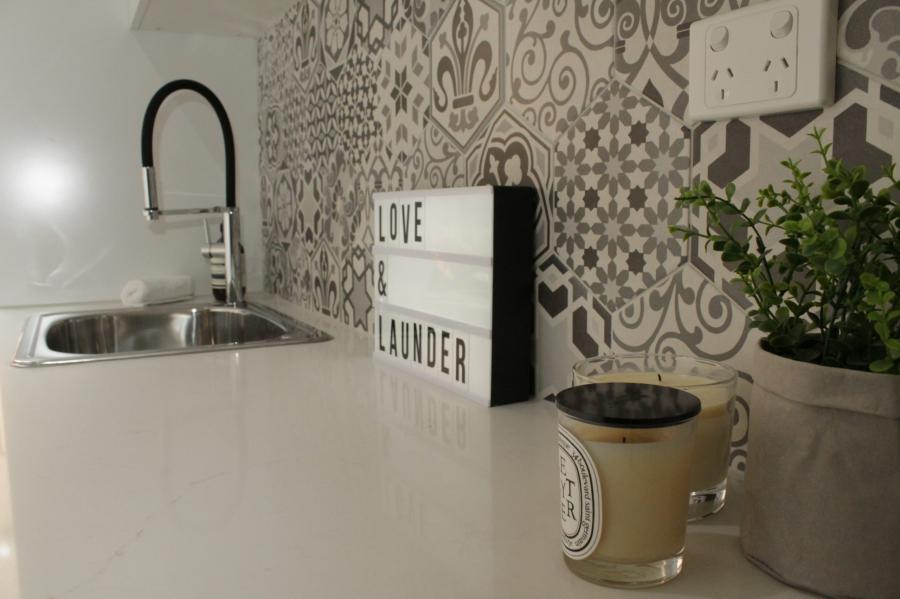 Laundry bench with sink, patterned tile splashback, plant and sign
