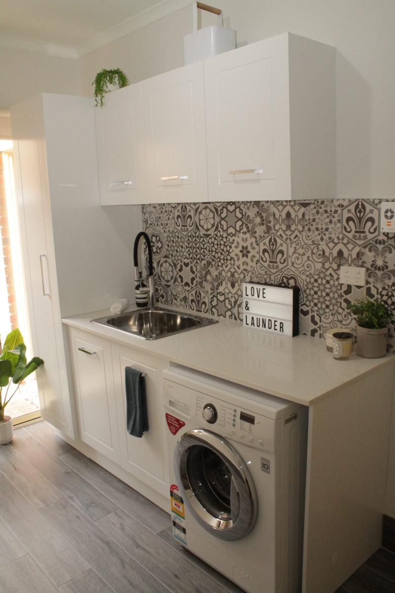 Compact modern laundry with white cabinetry, front-load washer and patterned splashback tiles